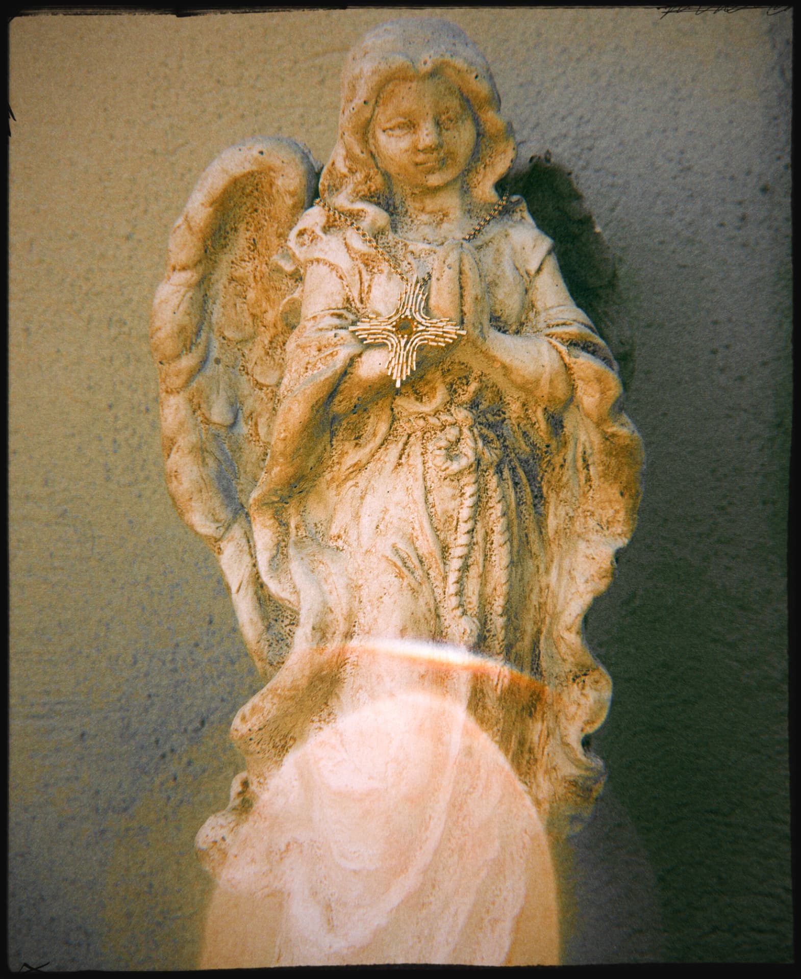 A stone angel in prayer wearing a gold sunburst cross