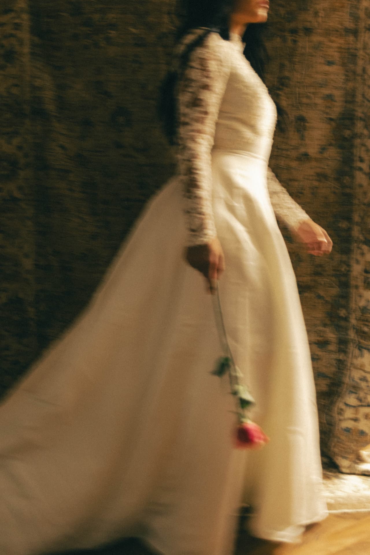 A bride walking in profile holding a single rose